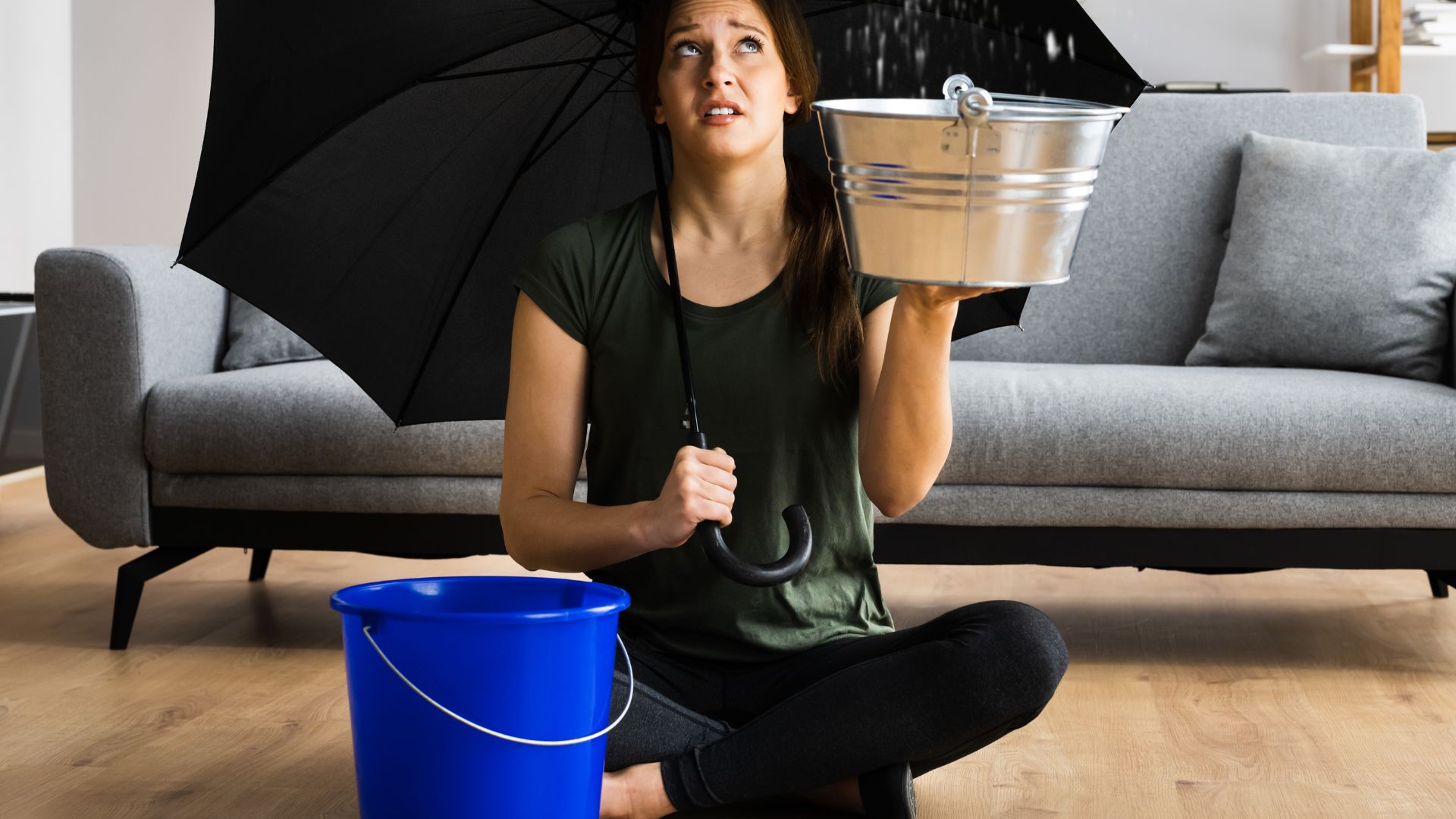Image of a woman holding an umbrella, and a bucket catching water from the roof