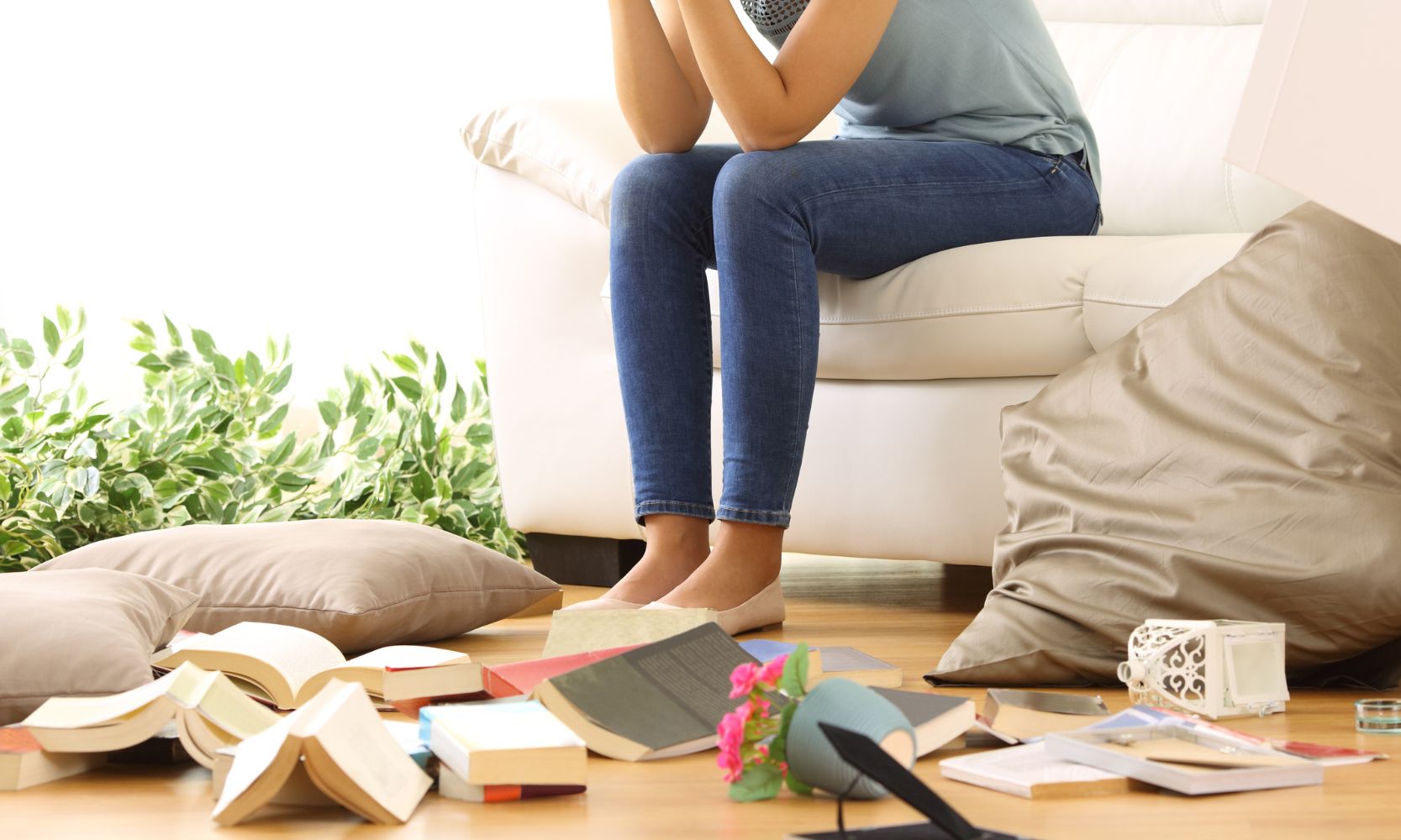 Image of a woman, holding her head, sad sitting on the couch while her apartment is damaged from a theft