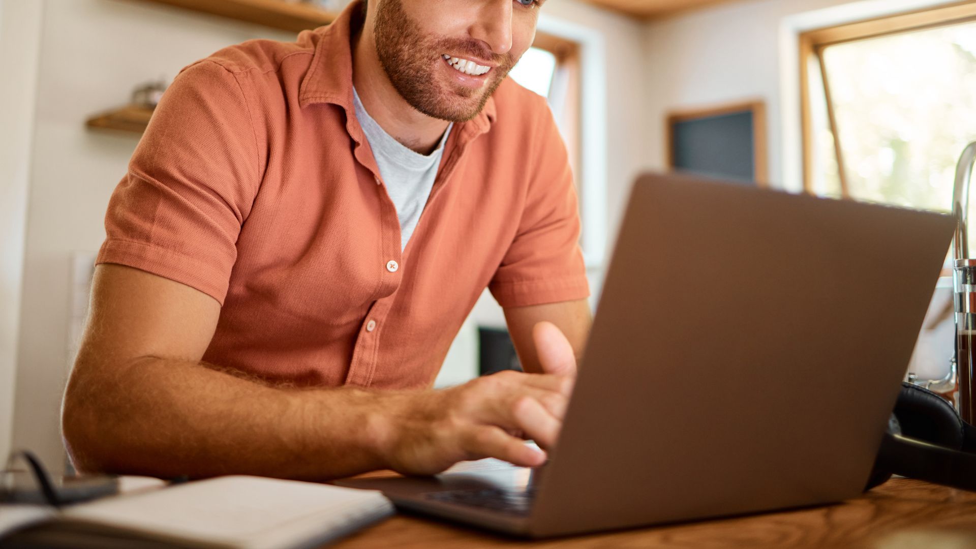 Image of a man looking at his laptop, smiling at a desk