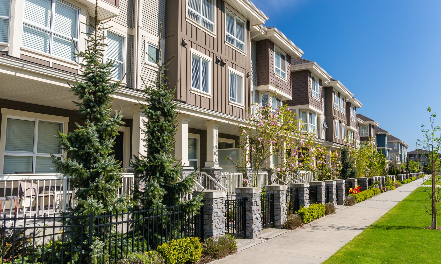A row of suburban condos with front patios and a tree-lined sidewalk