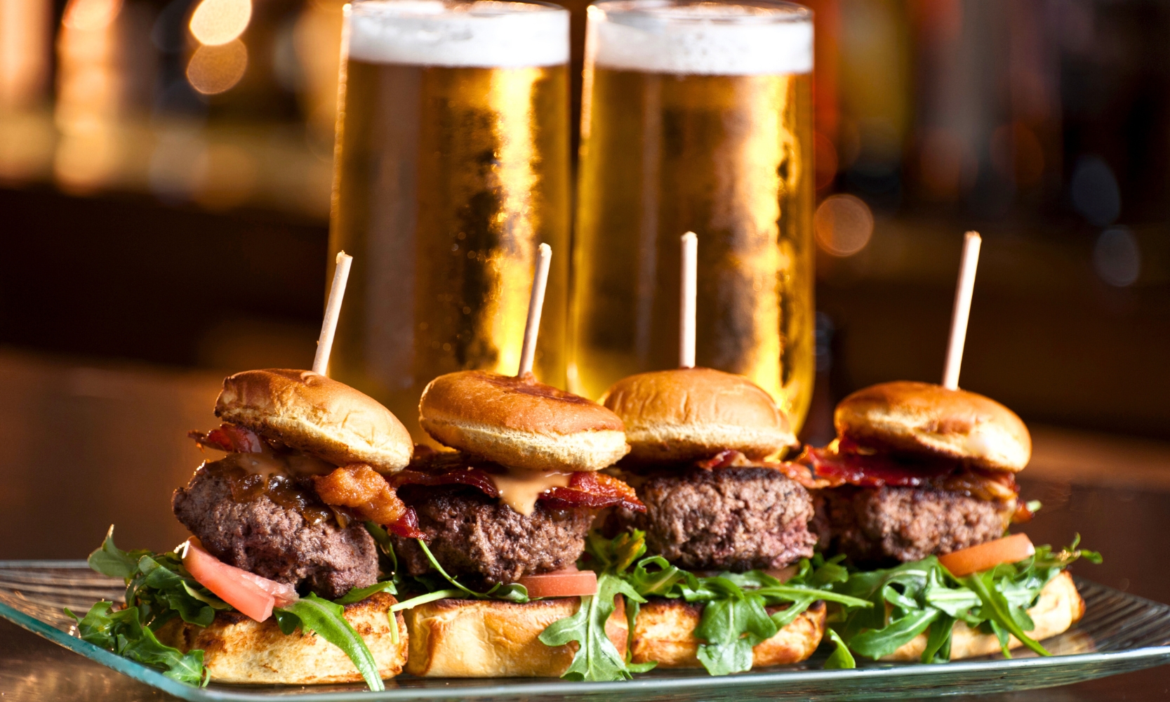An image of four mini burgers and two pint beers at a brewery