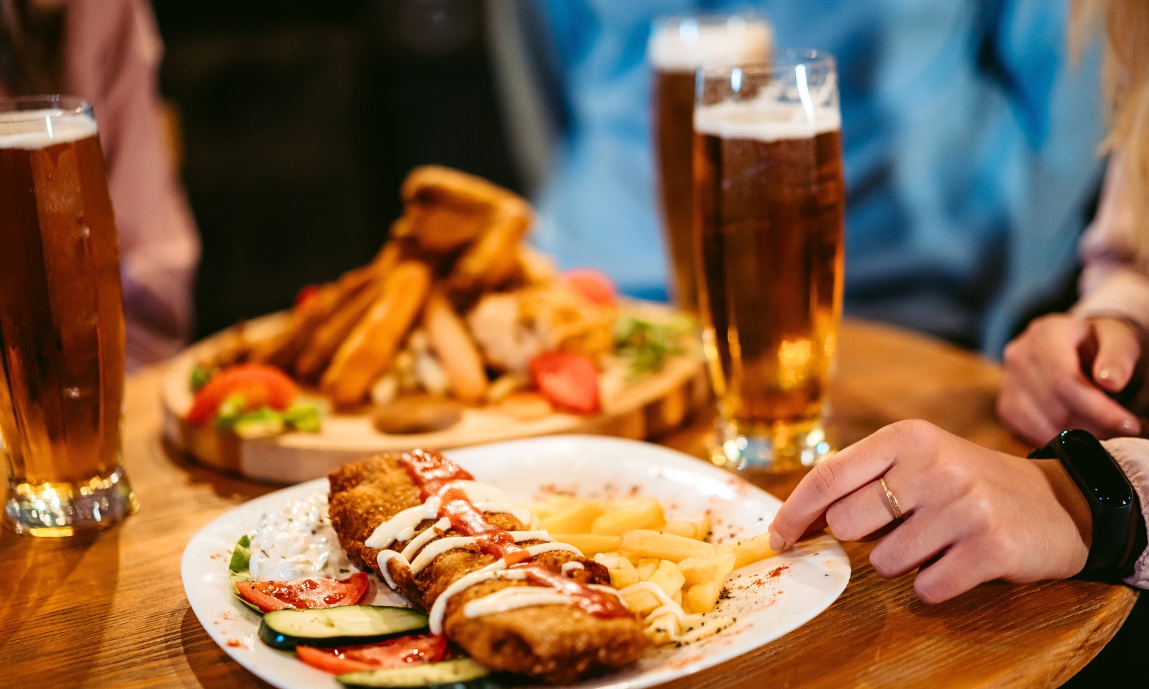 A closeup image of people eating at a pub with beers and entrees