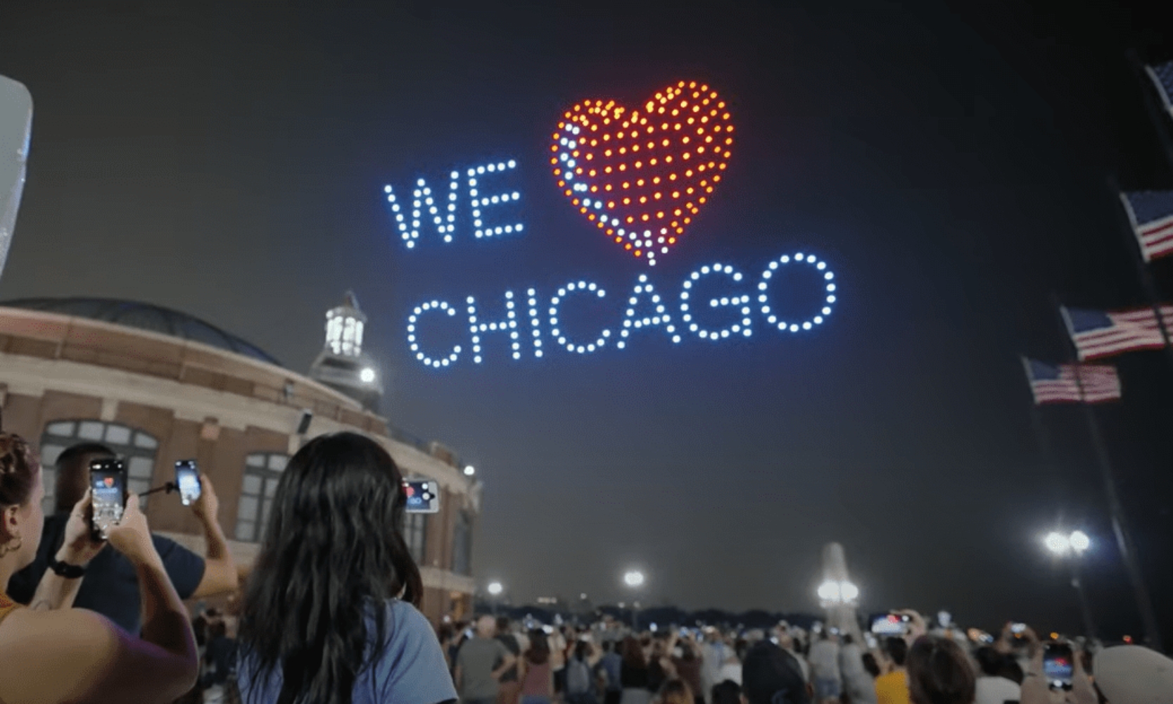 People looking at a drone night show at Navy Pier with lights showing We Love Chicago