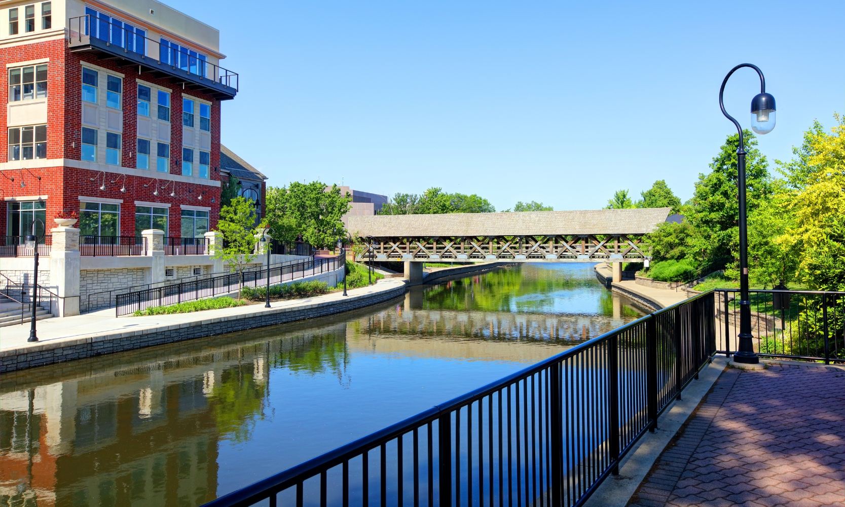 Image of the Naperville Riverwalk with a bridge, river, red building, and walkway path