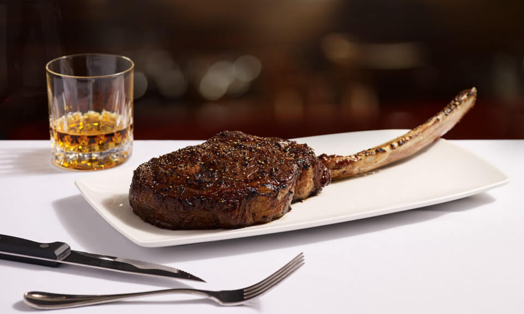 A closeup image of a bone-in steak entree and whiskey glass at Sullivan's Steakhouse