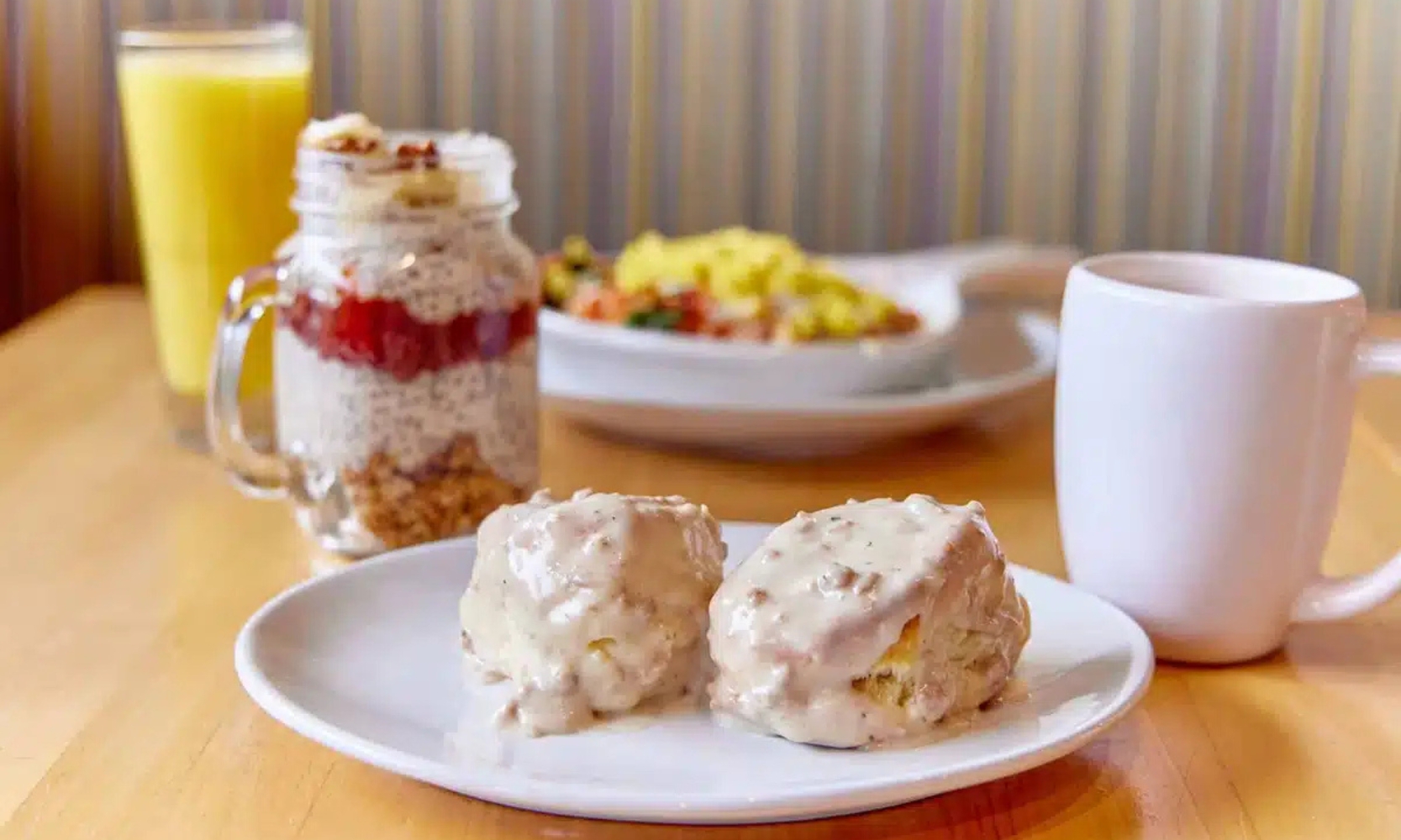 Image of a biscuits with gravy, parfait mug, egg entree, coffee mug, and orange juice at Honey Biscuit in Arlington Heights, IL