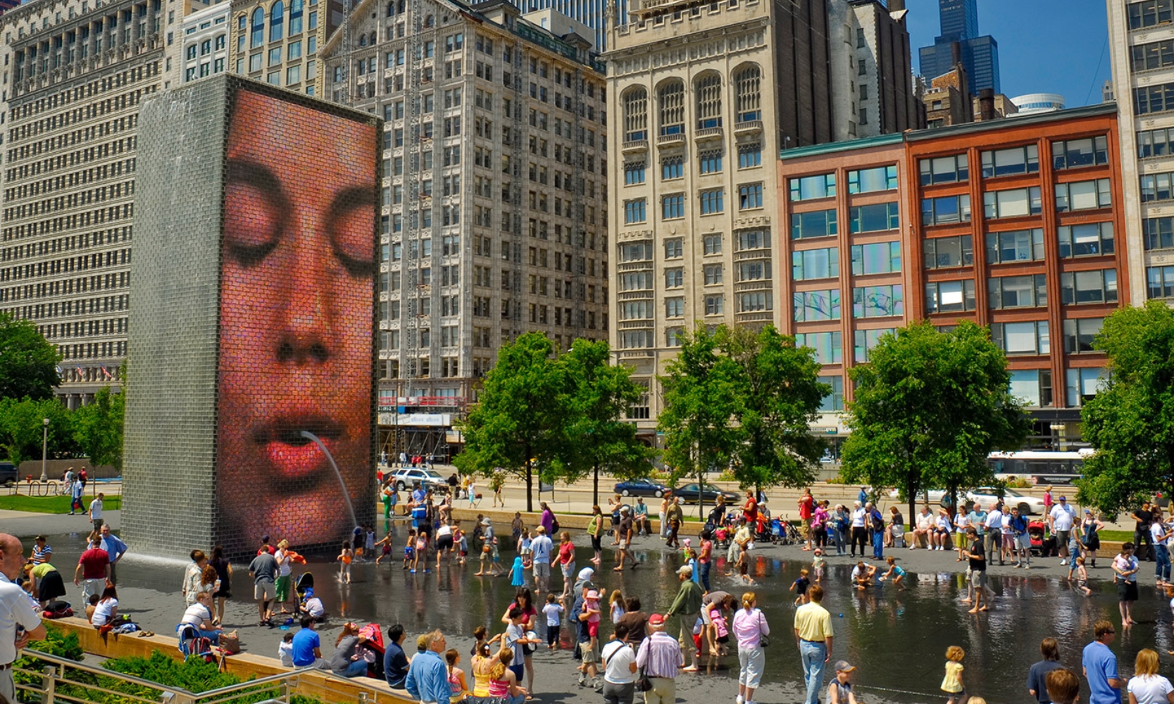 Image of the Millennium Park Crown Fountain with people in the water and the LCD display pouring water out a person's mouth