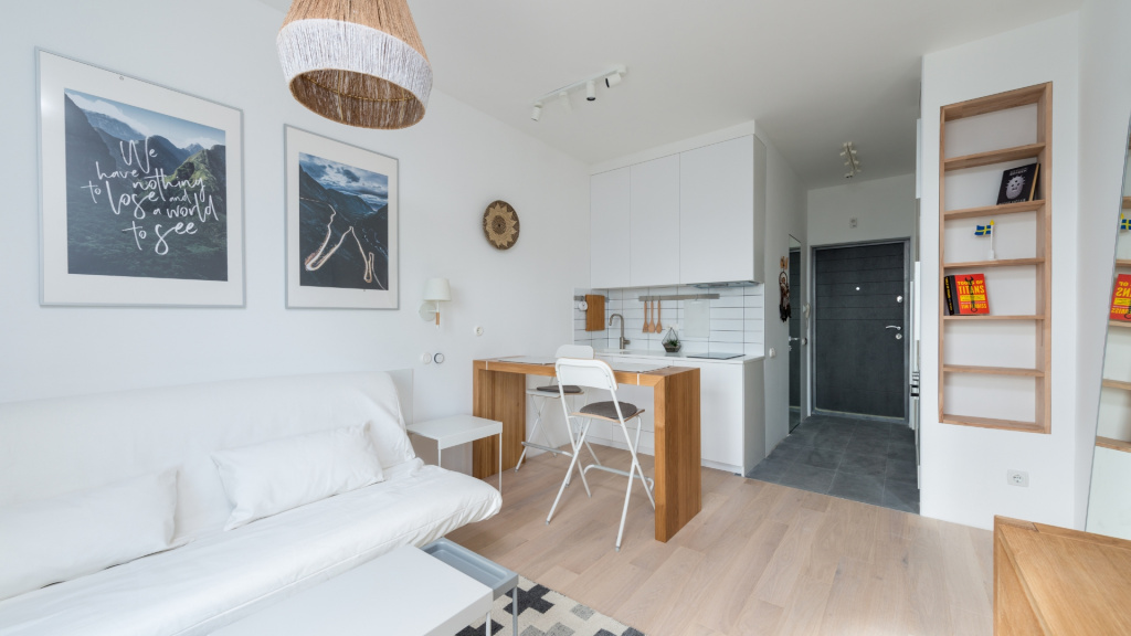 Wide shot image of a small white apartment with wooden accents, hanging wall art, and furniture