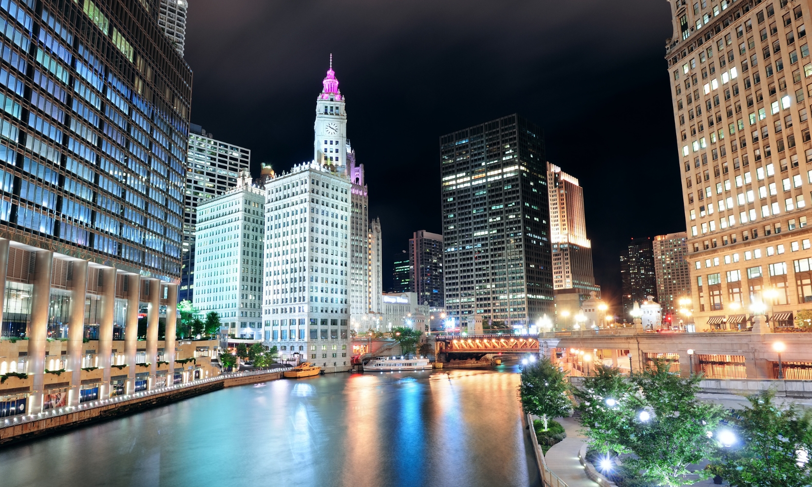 Nighttime photo of the Chicago Riverwalk illuminated at night with surrounding buildings