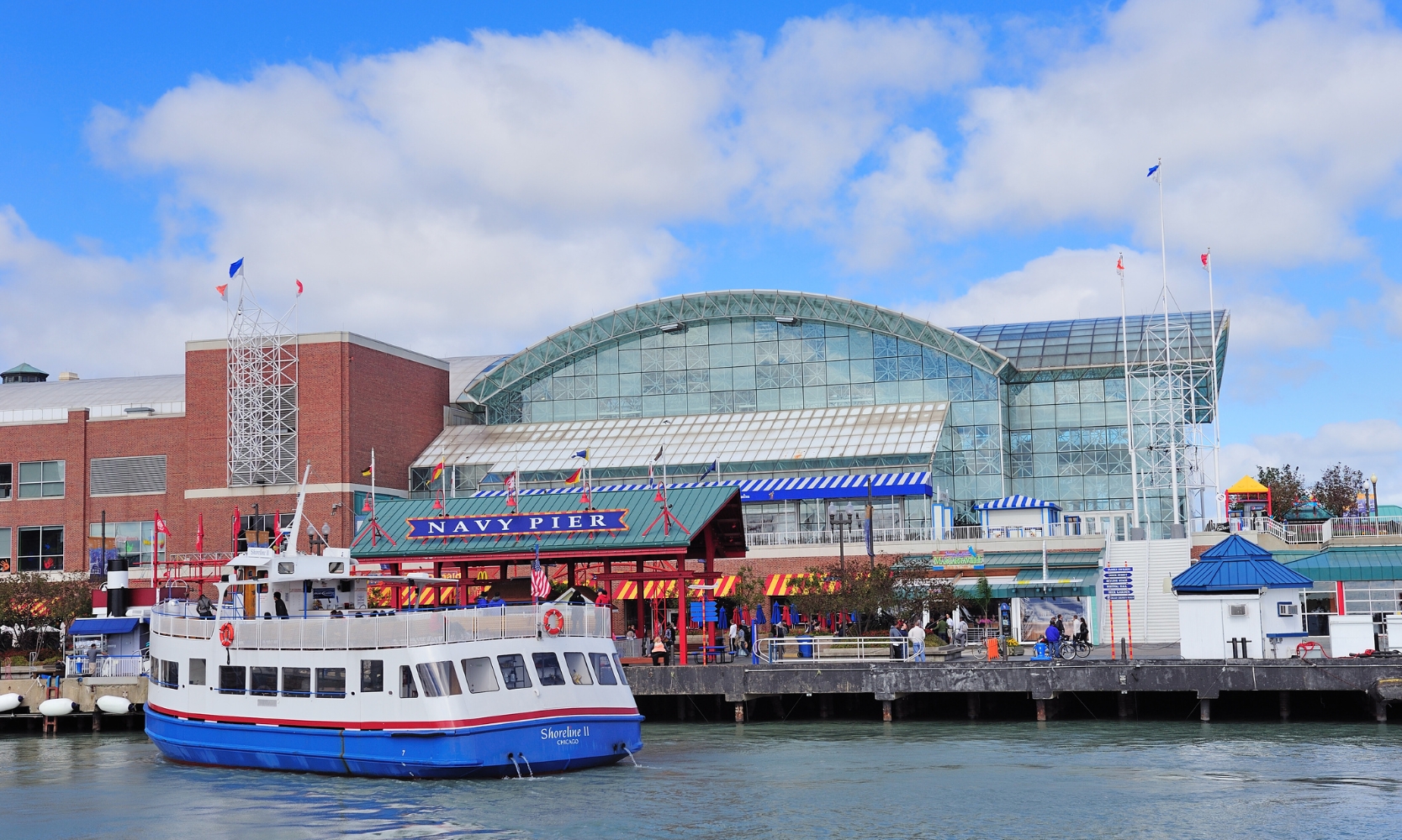 Image of Chicago's Navy Pier with a ferry boat on the water and people walking around during the day