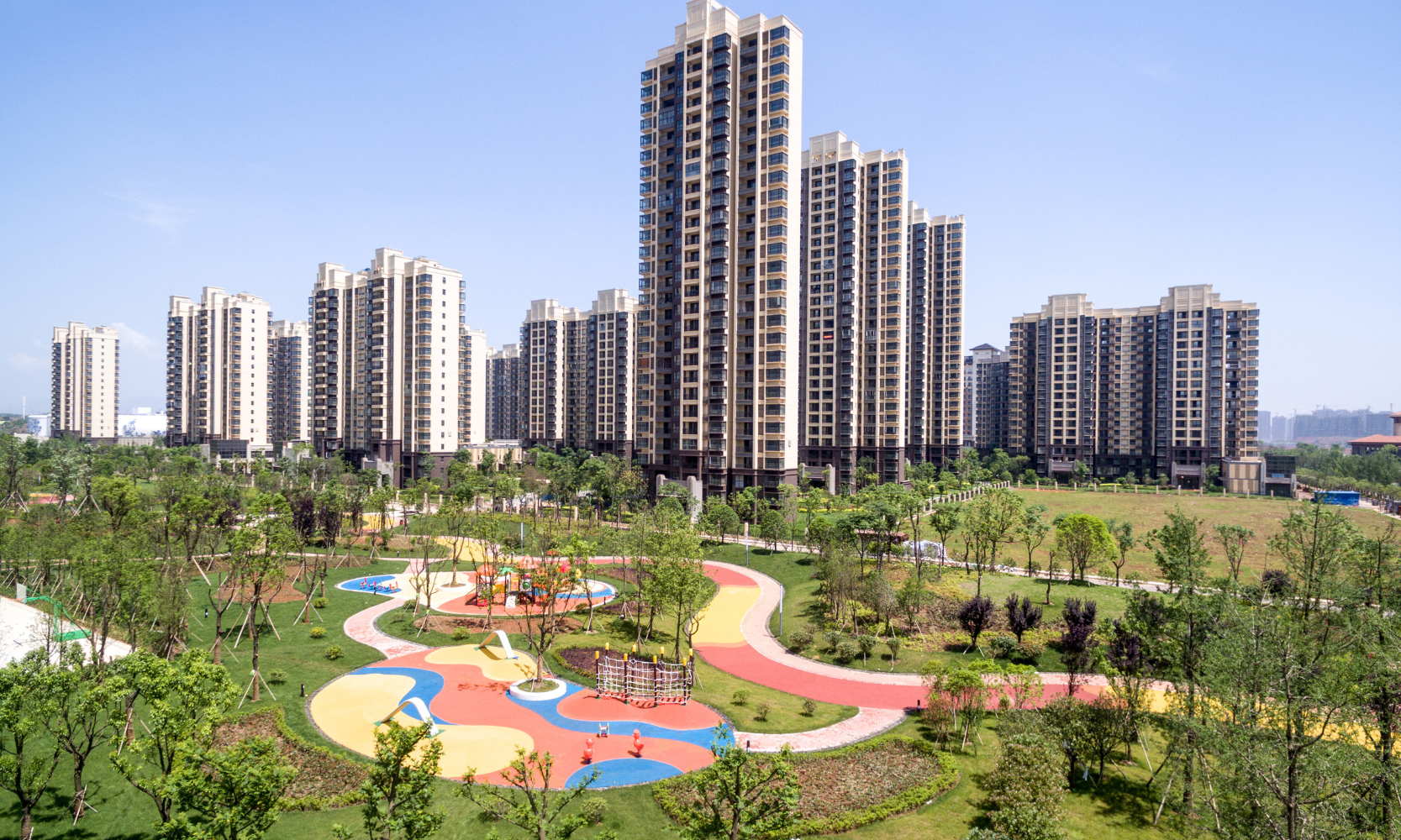 Exterior wide shot image of high-rise apartment buildings overlooking a children's playground at a park with trees surrounding