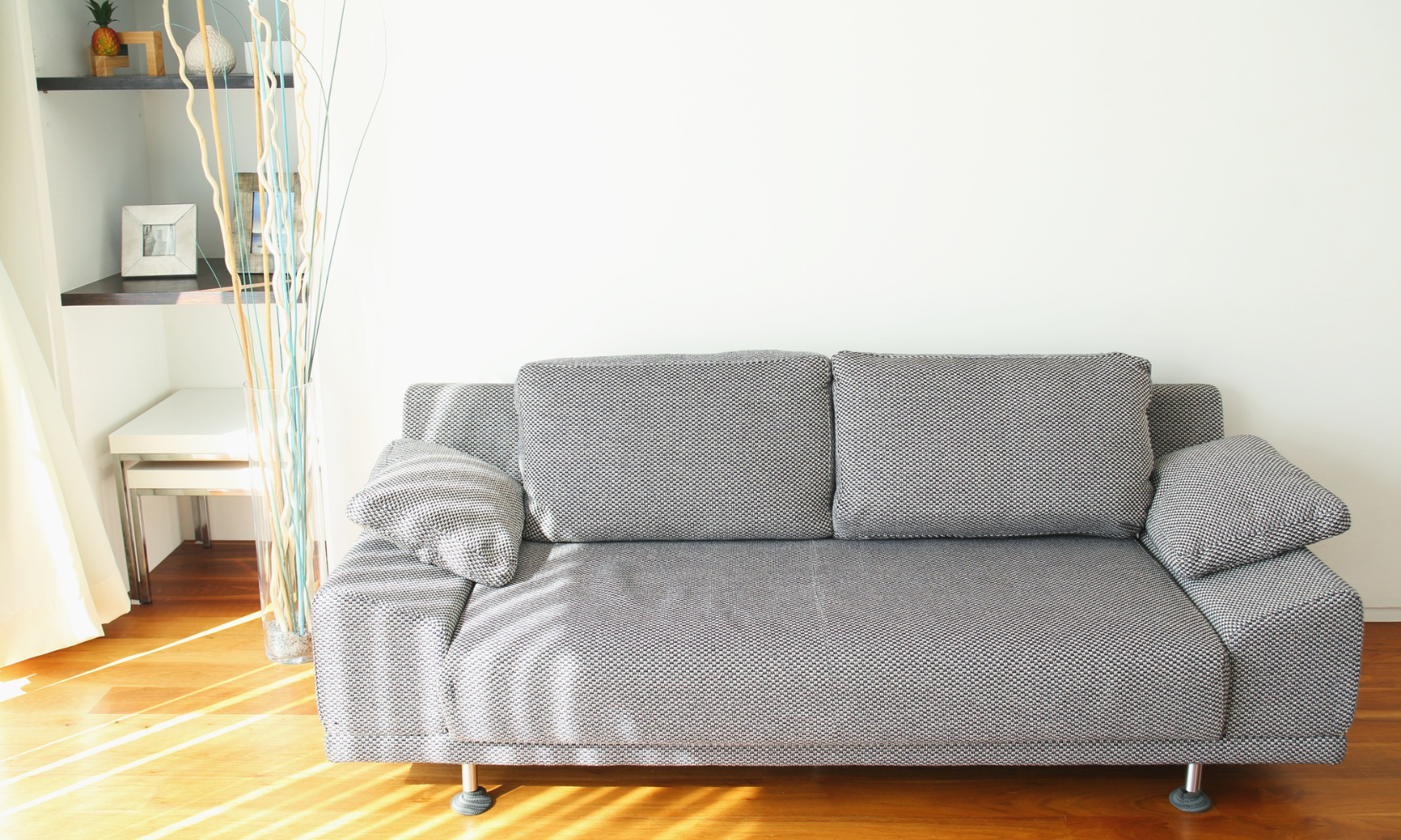 Image of a gray linen couch on a wooden floor next to wall shelves in an apartment