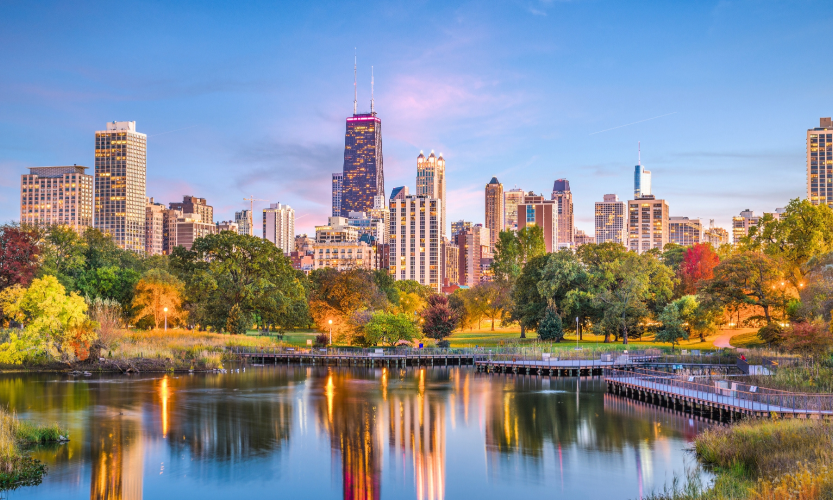 Wideshot image of Lincoln Park, Chicago, with illuminated skyscapers and water as sunset